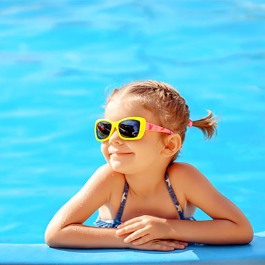 Lächelndes Kleinkind am Rand eines Pools. Je nach Härte des Poolwassers kann es zu Schäden an Oberflächen und zu Korrosion in Rohren kommen.